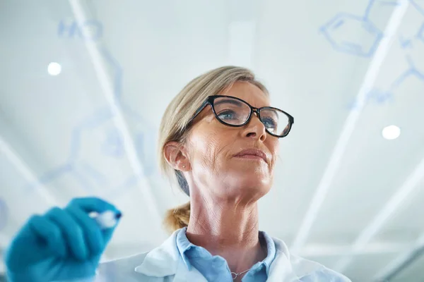 Vetenskapen är en av de viktigaste kunskapskanalerna. Skott av en mogen forskare som ritar molekylära strukturer på en glasvägg i ett labb. — Stockfoto