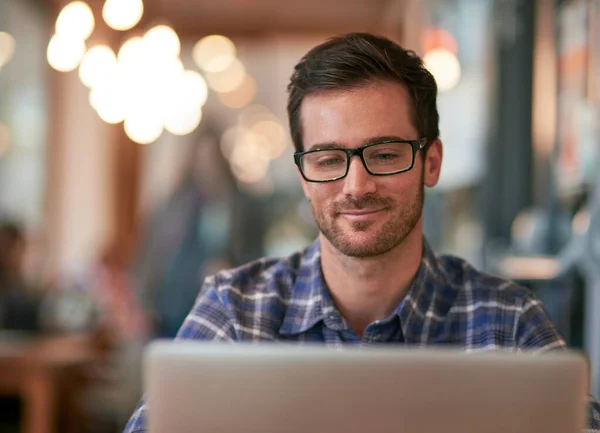 The free wifi here makes it a no brainer. Shot of a young man using his laptop while sitting in a coffee shop. — ストック写真