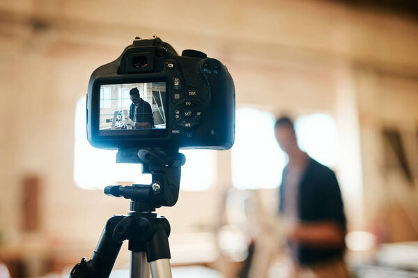 Hes all set to get the tutorial under way. Shot of young carpenter recording a tutorial of him making a wooden masterpiece on a video camera inside his workshop.