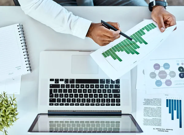 Was sagen Ihre Unternehmensdaten aus? Hochwinkelaufnahme eines nicht wiederzuerkennenden Geschäftsmannes, der Papierkram erledigt, während er in einem Büro an einem Laptop arbeitet. — Stockfoto