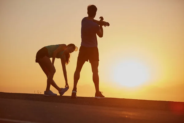 Feeling the burn and loving it. Shot of a silhouetted couple out for a run at sunrise. — Stock Photo, Image