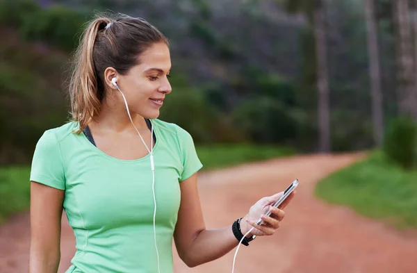 Getting the perfect playlist lined up for her run. Shot of a young woman listening to music while out running. — ストック写真
