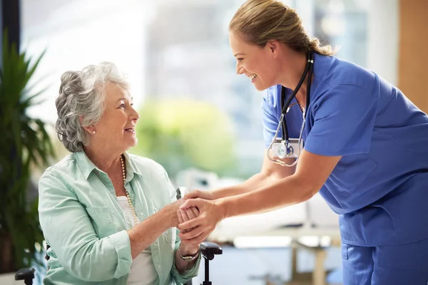Ze kan goed overweg met haar patiënten. Schot van een dokter die handen schudt met een lachende oudere vrouw in een rolstoel. — Stockfoto