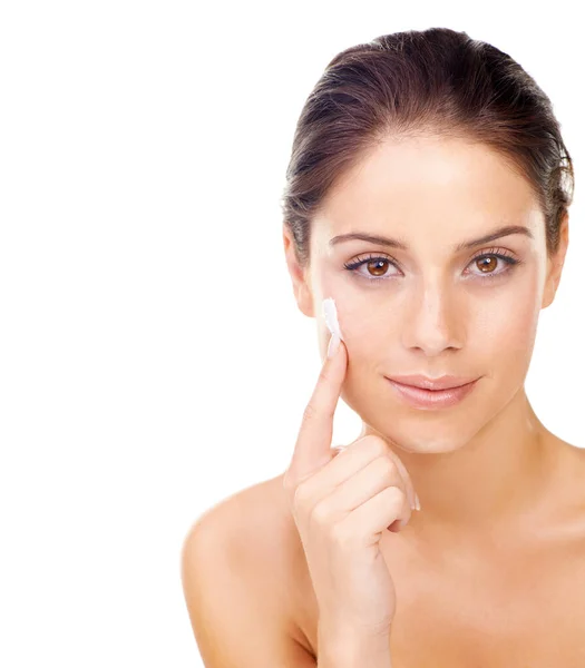 Maintaining beauty. Studio portrait of a beautiful young woman applying a skincare product to her face. — ストック写真