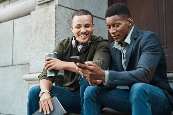 Lavora dove ti motiva a far accadere le cose. Foto di due giovani uomini d'affari che utilizzano uno smartphone insieme su uno sfondo urbano. — Foto Stock