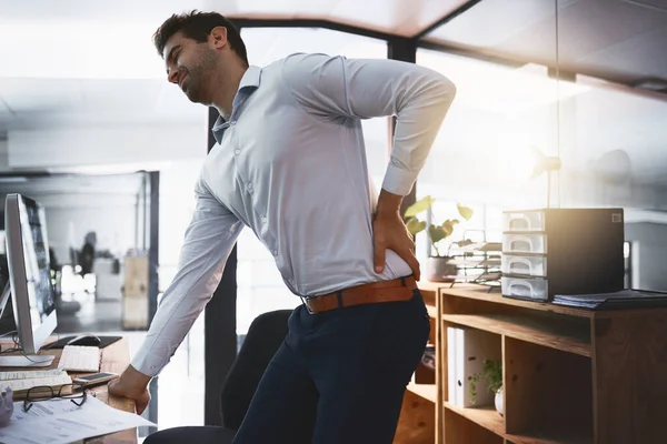 Diese Risse klingen nicht gut. Aufnahme eines jungen Geschäftsmannes, der unter Rückenschmerzen leidet, während er spät im Büro arbeitet. — Stockfoto