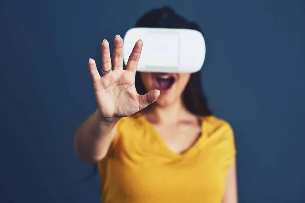 Megváltoztatni a valóság arcát. Stúdió portré egy vonzó fiatal nőről, aki VR headsetet visel kék háttérrel. — Stock Fotó
