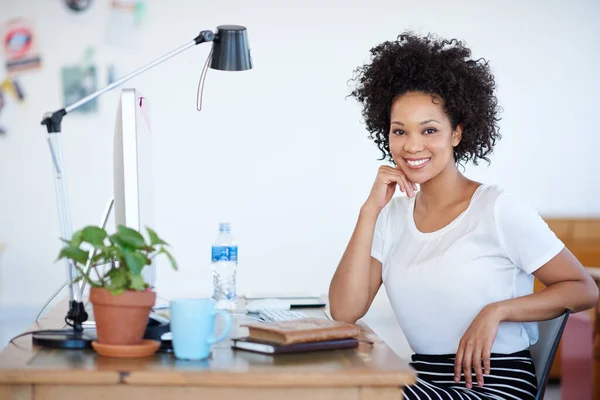 Portrait of an attractive young woman sitting at her workstation in the office. The commercial designs displayed in this image represent a simulation of a real product and have been changed or altered