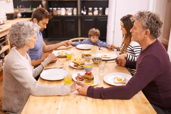 Благослови эту пищу нашим телам. Обрезанный снимок семьи, произносящей молитву перед завтраком. — стоковое фото