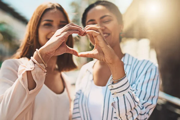 L'amore mantiene forti le tue amicizie. Girato di due giovani donne allegre che formano una forma di cuore con le mani unite mentre stanno fuori durante il giorno. — Foto Stock