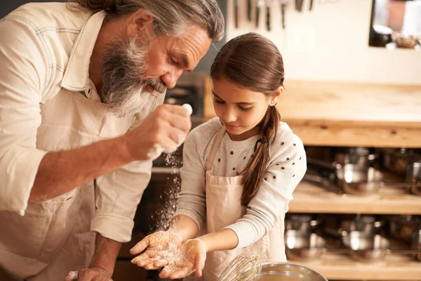 Adicionando um pouco mais. Tiro de uma garota se unindo com seu avô como eles assar na cozinha. — Fotografia de Stock