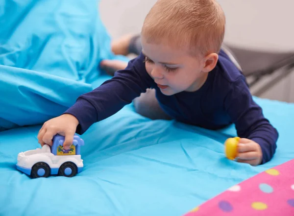 Vrooommmm. Un niño jugando con un coche de juguete en su cama. — Foto de Stock
