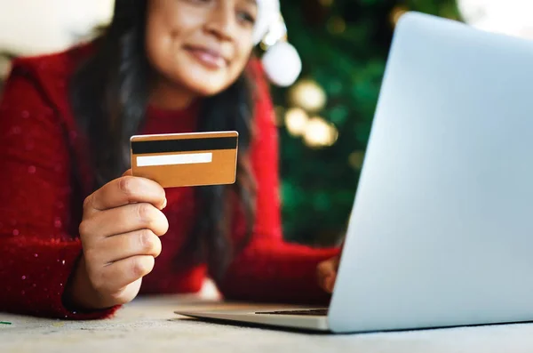 Shop online, save Santa some time. Shot of a happy young woman using a laptop and credit card during Christmas at home.