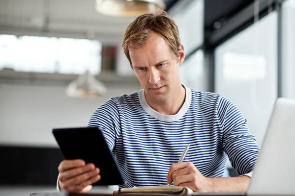Modern mai multitasking. Egy digitális táblagépen és laptopon dolgozó férfiról készült felvétel egy irodában.. — Stock Fotó