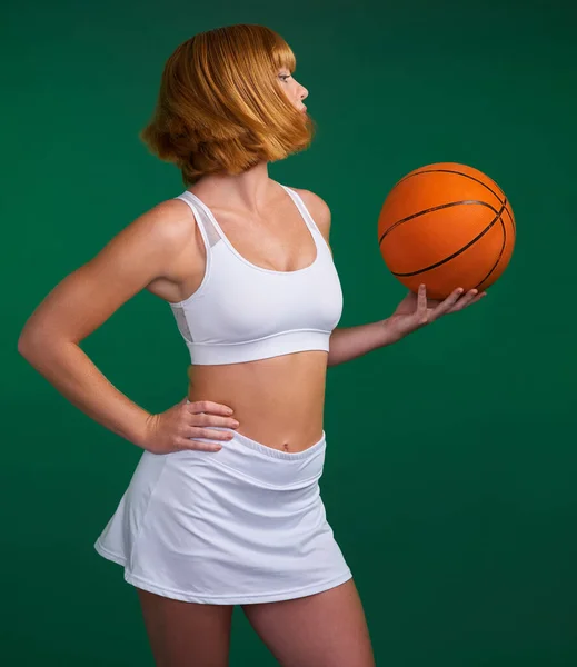 为进步而奋斗。拍下了一个年轻迷人的女运动员独自站在演播室里，拿着一个绿色背景的篮球. — 图库照片