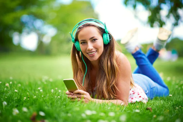 La musique et la nature sont si bonnes pour l'âme. Prise de vue d'une jeune femme écoutant de la musique alors qu'elle était allongée sur l'herbe du parc. — Photo