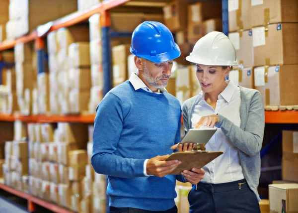 Comparing notes for accuracy. Shot of two people doing an inventory check in a warehouse. — Stock Photo, Image