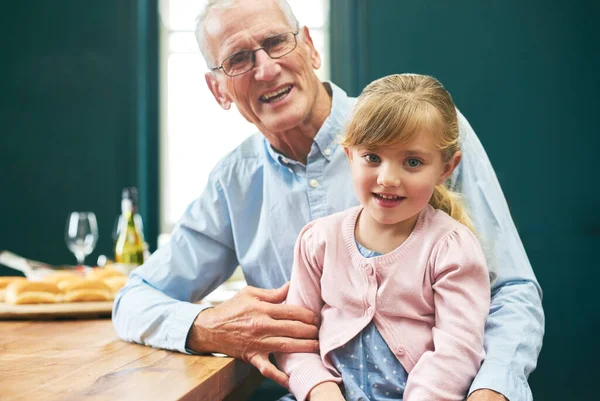 Nejstarší a nejmladší z rodiny. Portrét veselého staršího muže a jeho vnučky, jak si hrají na digitálním tabletu vedle stolu doma. — Stock fotografie