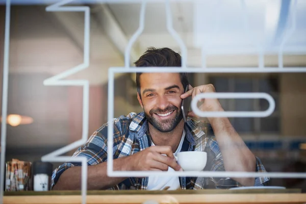 Mantenerse conectado durante su pausa para el café. Retrato de un joven feliz contestando su celular mientras tomaba café en su cafetería favorita. — Foto de Stock