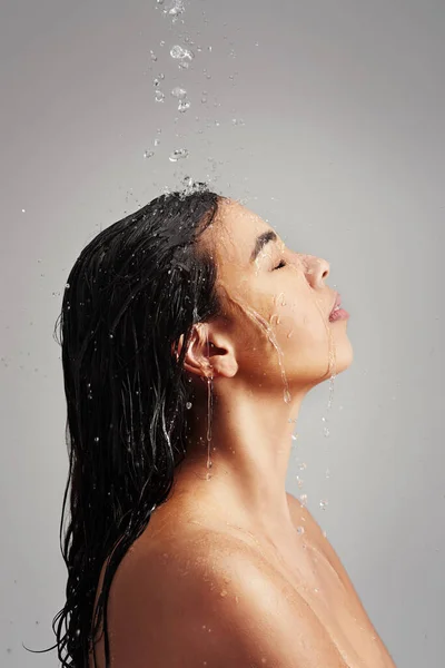 Wat een geweldige manier om de dag te beginnen. Studio shot van een jonge vrouw genieten van een douche tegen een grijze achtergrond. — Stockfoto