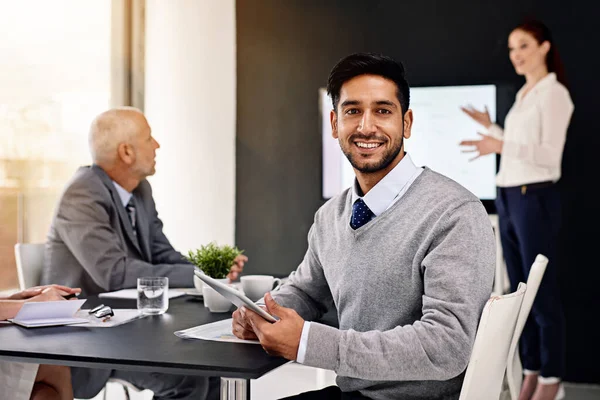 Energin på det här kontoret är otrolig. Porträtt av en ung affärsman som sitter i styrelserummet med kollegor i bakgrunden. — Stockfoto