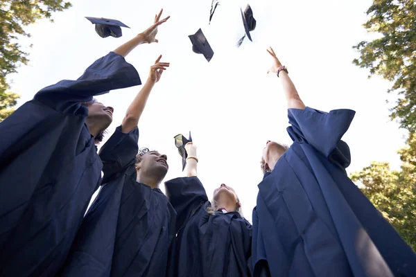 A kemény munkánk kifizetődött. Egy csapat diplomás ünnepel azzal, hogy feldobják a kalapjukat az égre.. — Stock Fotó