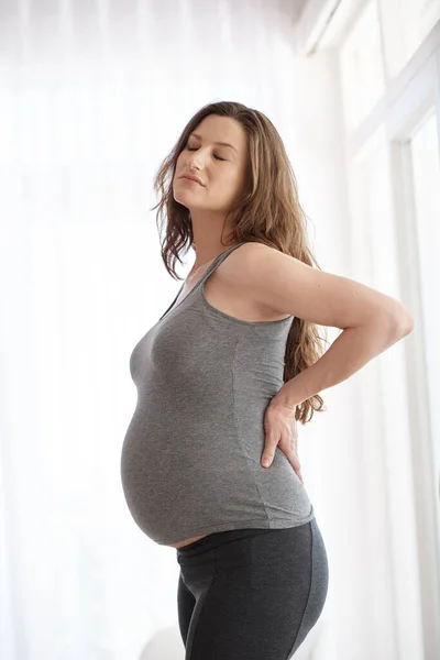 Aches and pains. Cropped shot of a young pregnant woman placing her hands on her lower back in discomfort. — Stock Photo, Image