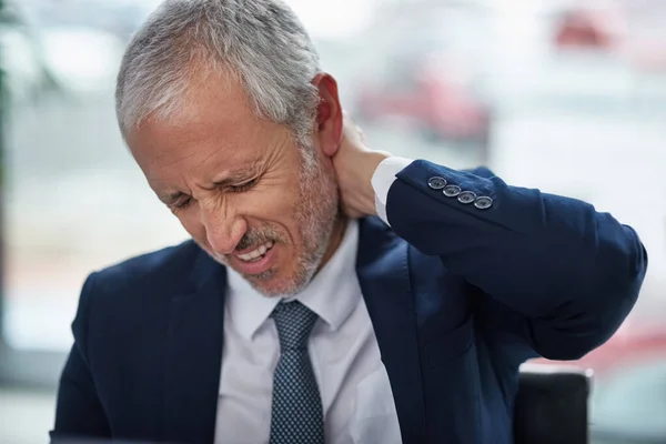 Los dolores y dolores del trabajo de oficina. Disparo de un hombre de negocios maduro que sufre de dolor de cuello mientras trabaja en una oficina. — Foto de Stock