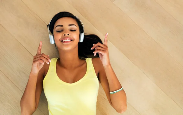 Adoro questa canzone. Colpo ad angolo alto di una giovane donna che ascolta musica sdraiata su un pavimento di legno. — Foto Stock