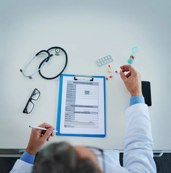 Setting the best treatment plan for his patients. High angle shot of an unrecognizable doctor busy with paperwork and medication in his office. — Stock Photo, Image