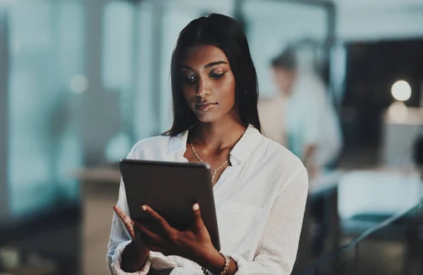 Und das alles auf einmal mit moderner Technik. Aufnahme einer jungen Geschäftsfrau mit einem digitalen Tablet in einem Büro in der Nacht. — Stockfoto