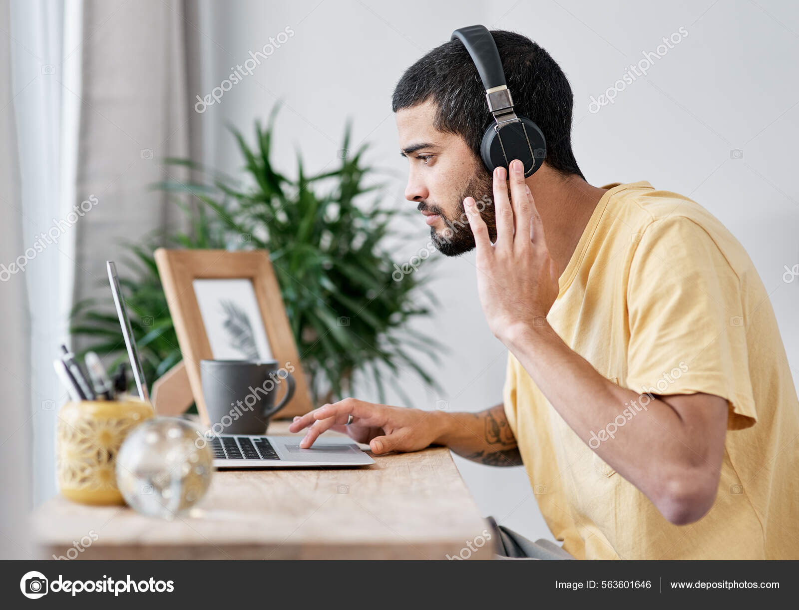 The best noise cancelling headphones in the business. Shot of a young man using a laptop and headphones while working from home. Stock Photo PeopleImages 563601646