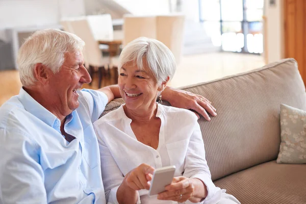 Es una forma más rápida de compartir mensajes divertidos. Fotografía de una pareja de ancianos usando un teléfono celular juntos. — Foto de Stock