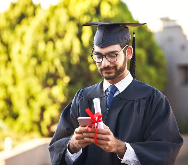 Colocando seu discurso de formatura online. Tiro de um jovem usando um telefone celular no dia da formatura. — Fotografia de Stock