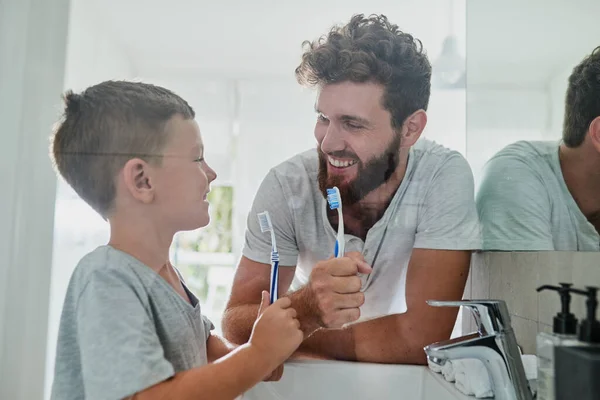 Tenemos que cuidar nuestros dientes. Un disparo de un padre y su hijo pequeño cepillándose los dientes juntos en el baño en casa. — Foto de Stock