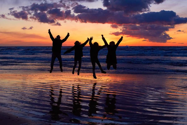 Die Vitalität der Natur lieben. Silhouette einer Gruppe von Menschen, die bei Sonnenuntergang am Strand springen. — Stockfoto