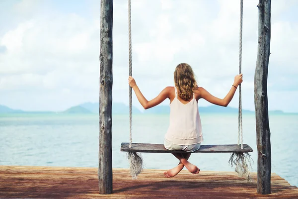Passar o dia no paraíso. Tiro de uma jovem mulher sentada em um balanço com vista para o oceano. — Fotografia de Stock