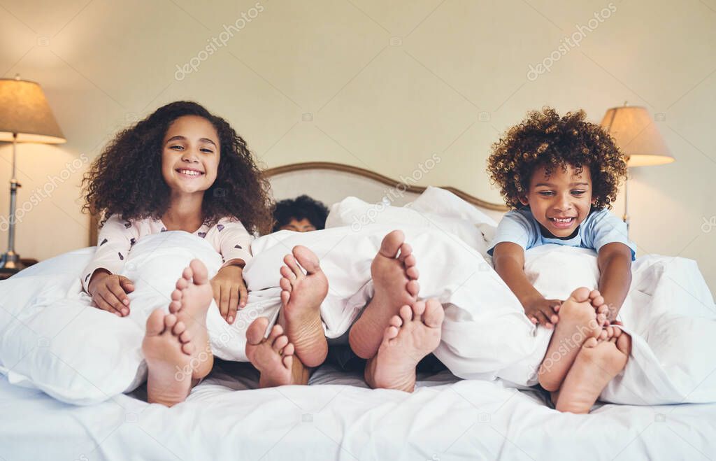 Were staying in but still having fun. Portrait of two adorable little children relaxing in bed with their parents at home.