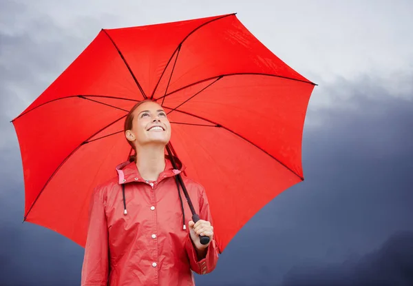 Jag är skyddad från väder och vind. En vacker ung kvinna som står utanför med sitt röda paraply. — Stockfoto