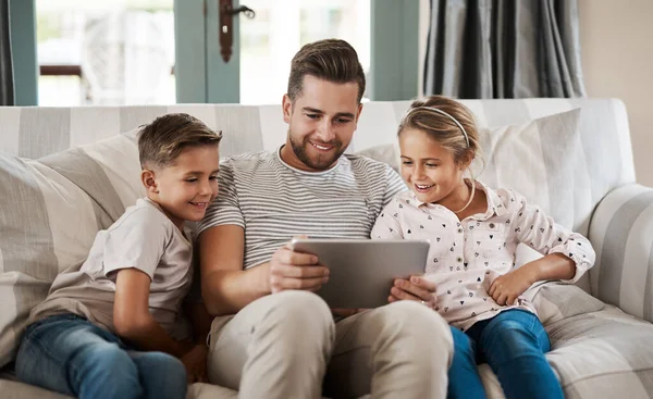 The go to gadget for learning time. Shot of an adorable little girl and boy using a digital tablet with their father on the sofa at home. — Stock Photo, Image