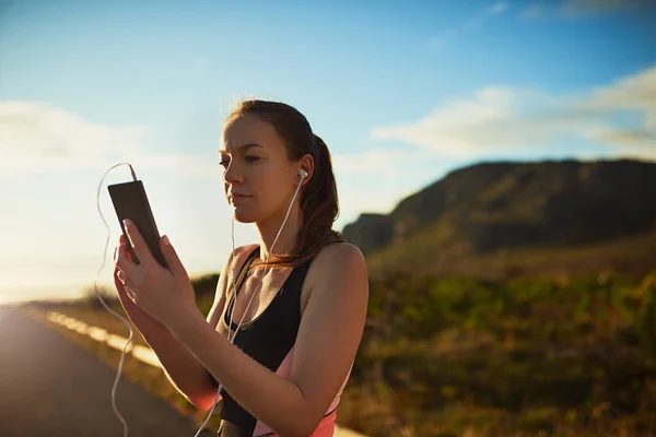 Getting her workout tracks ready. Shot of a sporty young woman organizing her workout playlist outdoors. — ストック写真