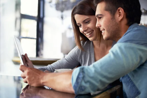 Olhando para seu álbum de fotos online. Tiro de um jovem casal olhando para um tablet digital enquanto sentado em um café. — Fotografia de Stock