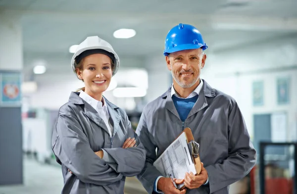 Gelukkig in ons beroep. Twee mensen met een harde hoed die glimlachen naar de camera in een fabriek. — Stockfoto