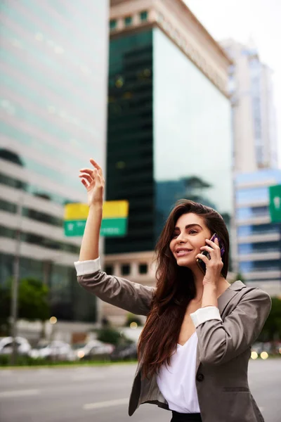 Aspetta, sto chiamando un taxi. Colpo ritagliato di una giovane donna d'affari attraente che chiama un taxi mentre prende una telefonata in città durante il giorno. — Foto Stock