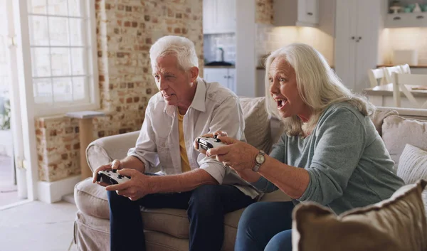 ¿Cómo hiciste eso? Toma de una pareja de ancianos sentados en el sofá en casa juntos y jugando. — Foto de Stock