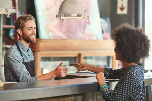 A conveniência do crédito. Tiro de um barista recebendo um pagamento de cartão de crédito de um cliente em um café. — Fotografia de Stock