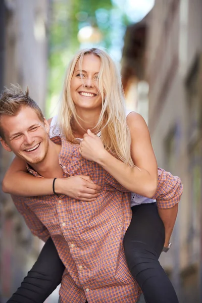 Having fun in the streets. A young man giving his beautiful girlfriend a piggyback ride in the street. — ストック写真