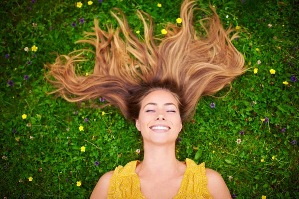 Quando sei felice tutti i giorni è una buona giornata di capelli. Colpo ad angolo alto di una giovane donna spensierata che si rilassa in un campo di erba e fiori. — Foto Stock