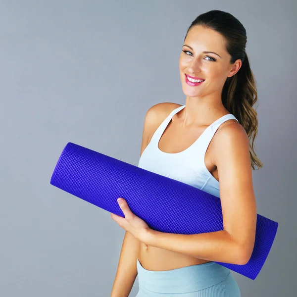 Vai para a aula de ioga. Retrato recortado de uma jovem atraente e desportiva carregando seu tapete de ioga contra um fundo cinza. — Fotografia de Stock