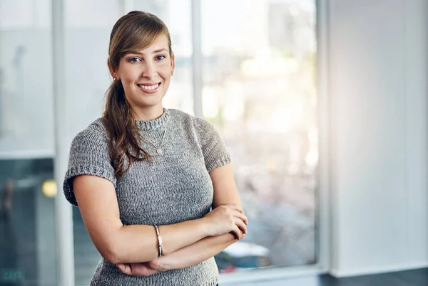 Młoda i zdeterminowana, by odnieść sukces. Portret pewnej siebie młodej bizneswoman stojącej z rękami złożonymi w biurze w pracy. — Zdjęcie stockowe